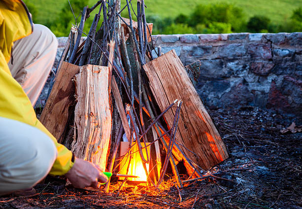 A person lighting up a TeePee style pile of wood